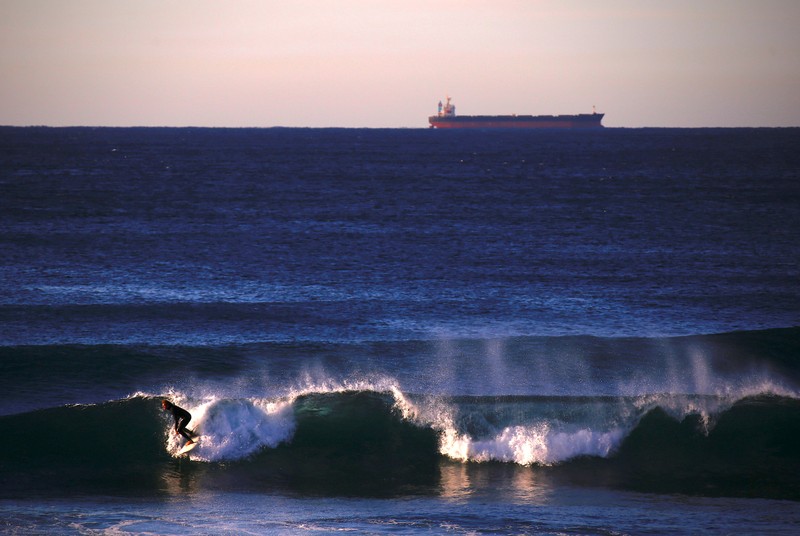 FILE PHOTO: A ship waiting to be filled with a load of coal can be seen behind a surfer riding a wave at Merewether Beach in Newcastle, located north of Sydney