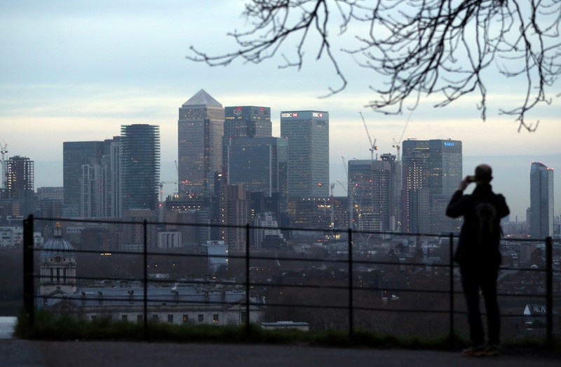 A man takes a photograph of the Canary Wharf financial district from Greenwich Park in London