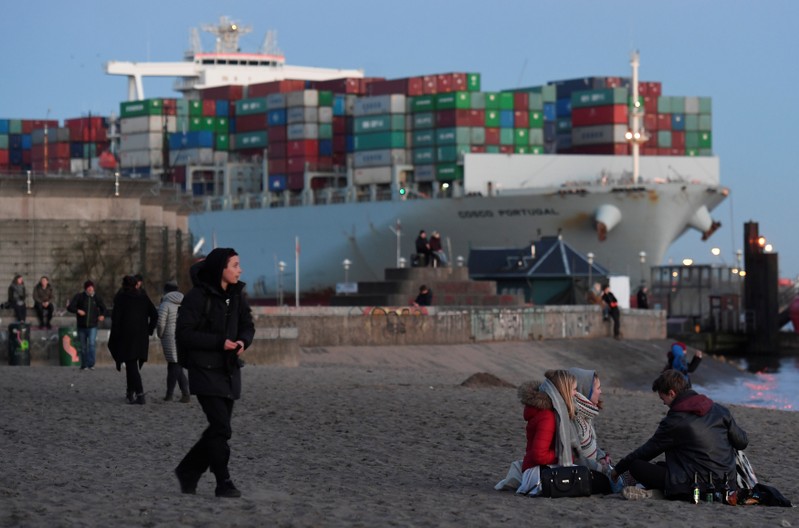 People enjoy the sunset in front of a container ship at the Elbe river in Hamburg