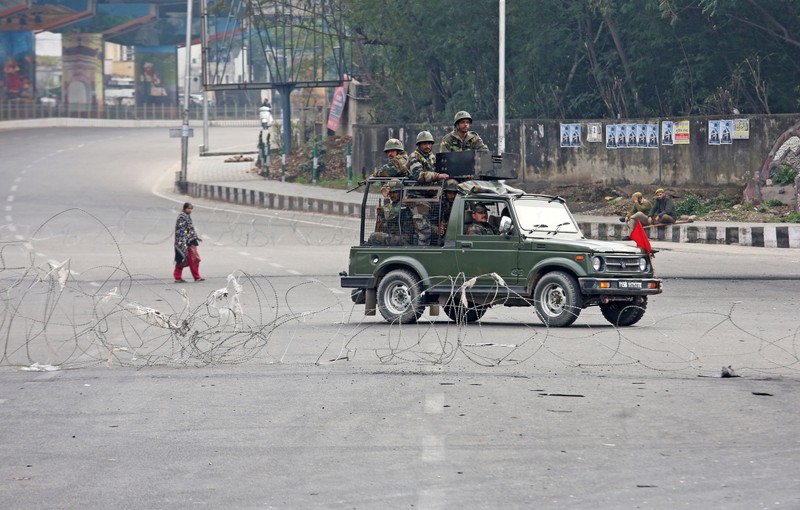 Indian Army soldiers in a vehicle patrol a street as a woman walks past during a curfew in Jammu