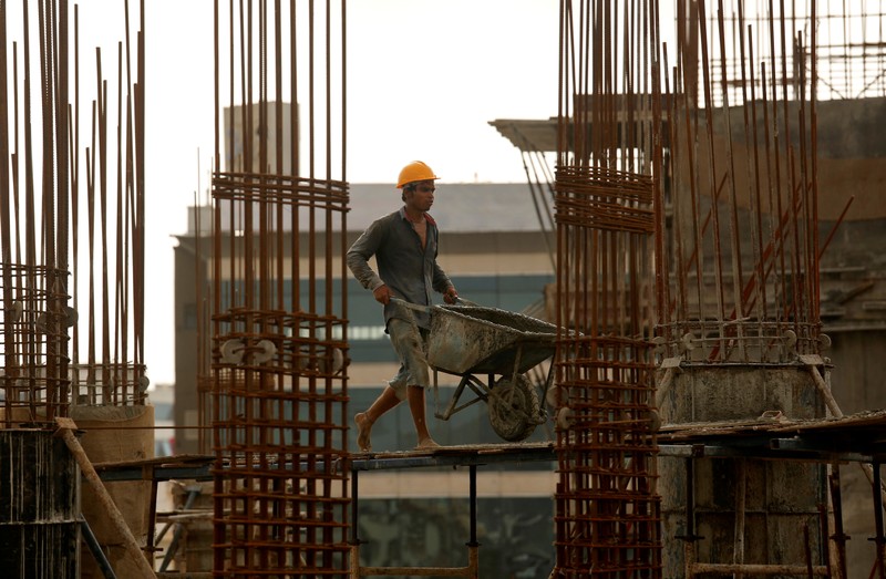 FILE PHOTO: A worker pushes a wheelbarrow to collect cement at a construction site of a residential building in Mumbai