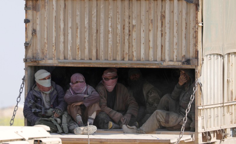 Men with covered faces sit in the back of a truck near the village of Baghouz