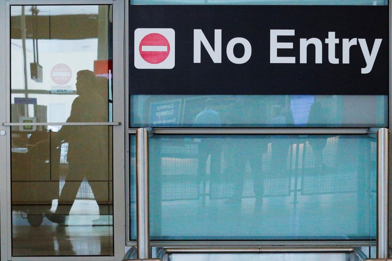 International travelers (reflected in a closed door) arrive on the day that U.S. President Donald Trump's limited travel ban, approved by the U.S. Supreme Court, goes into effect, at Logan Airport in Boston
