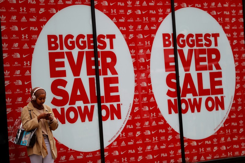 FILE PHOTO: A pedestrian stands in front of a shop displaying a sale sign, in central London