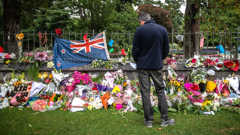 A man pauses next to a New Zealand flag hung amongst flowers and tributes on the wall of the Botanic Gardens, March 17, 2019, in Christchurch, New Zealand for the victims of a mass shooting at two mosques.