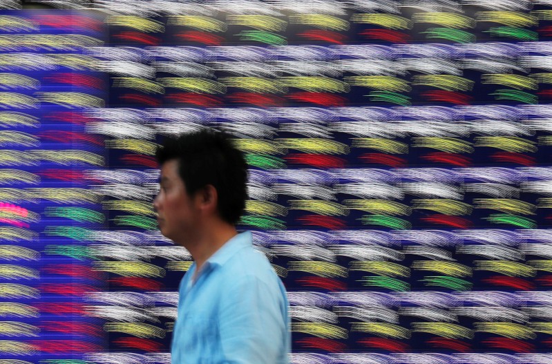 FILE PHOTO: Passersby walk past in front of an electronic stock quotation board outside a brokerage in Tokyo