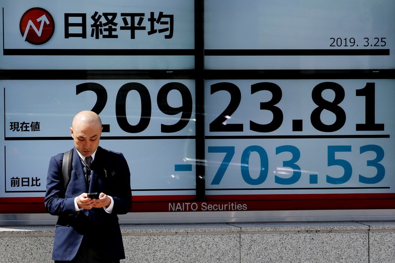 FILE PHOTO: A man stands in front of an electronic board showing the Nikkei stock index outside a brokerage in Tokyo