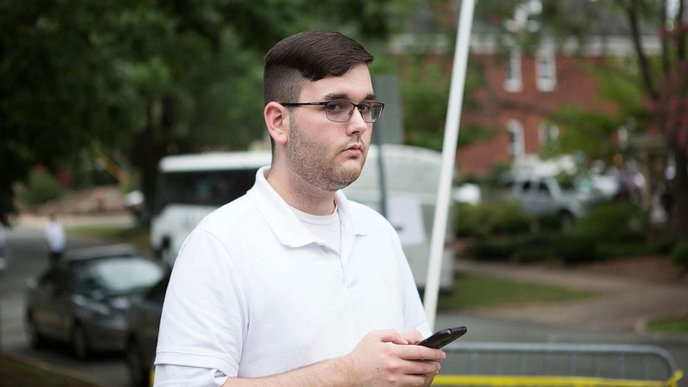 In this Saturday, Aug. 12, 2017, photo, James Alex Fields Jr. stands on the sidewalk looking at the procession of the clergy as they gathered at McGaffey park, ahead of a rally in Charlottesville, Va.