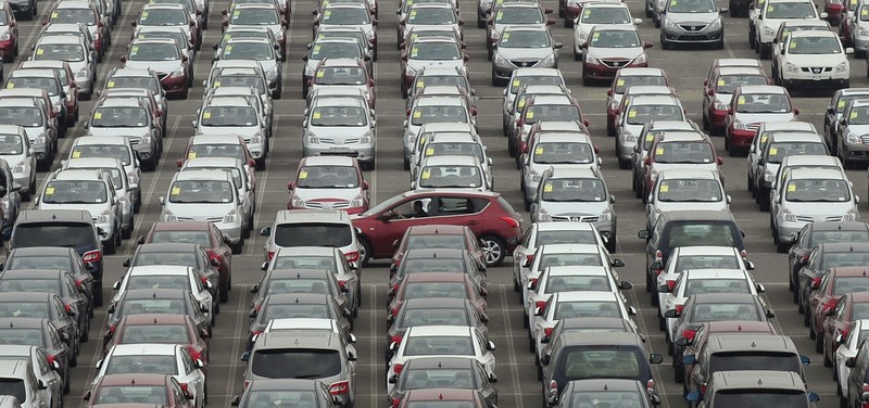 FILE PHOTO: Man drives red car past parking lot where large numbers of newly manufactured cars are parked at Dayaowan port of Dalian