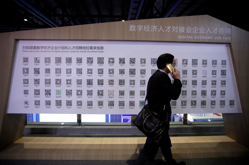 FILE PHOTO: A man walks past a poster showing the QR codes for job-seeking information during an internet expo at the fifth WIC in Wuzhen