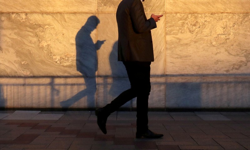 FILE PHOTO: An unidentified man using a smart phone walks through London's Canary Wharf financial district in the evening light in London