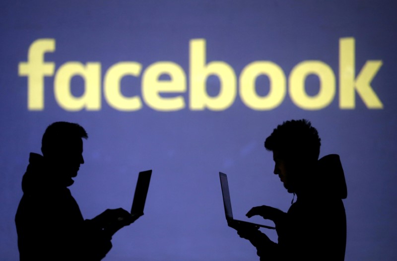 FILE PHOTO: Silhouettes of laptop users are seen next to a screen projection of Facebook logo in this picture illustration