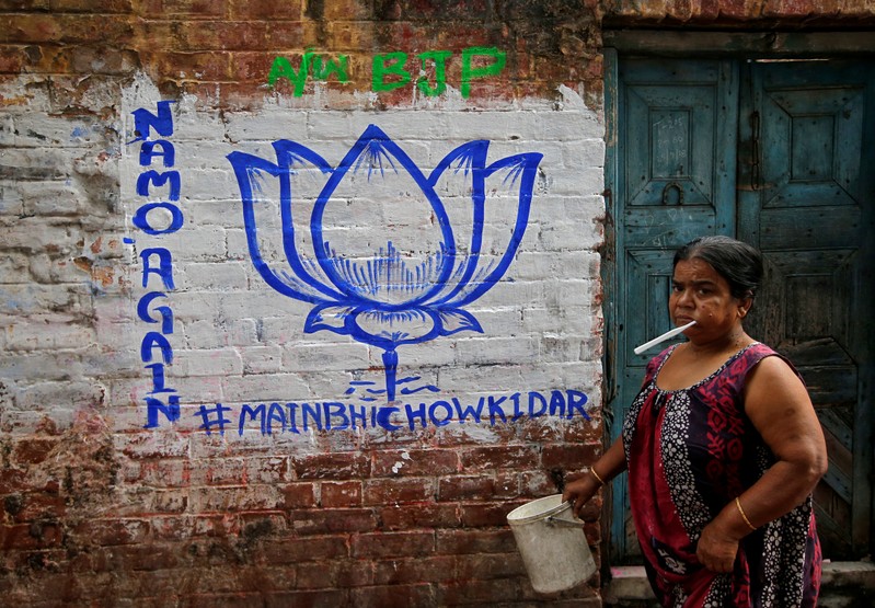 A woman walks past a wall painted with the election symbol of India's ruling Bharatiya Janata Party in an alley at a residential area in Kolkata