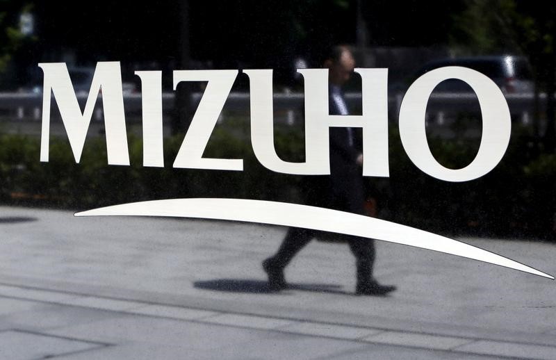 FILE PHOTO: Pedestrian is reflected in a sign showing the logo of the Mizuho Financial Group Inc. outside its headquarters in Tokyo