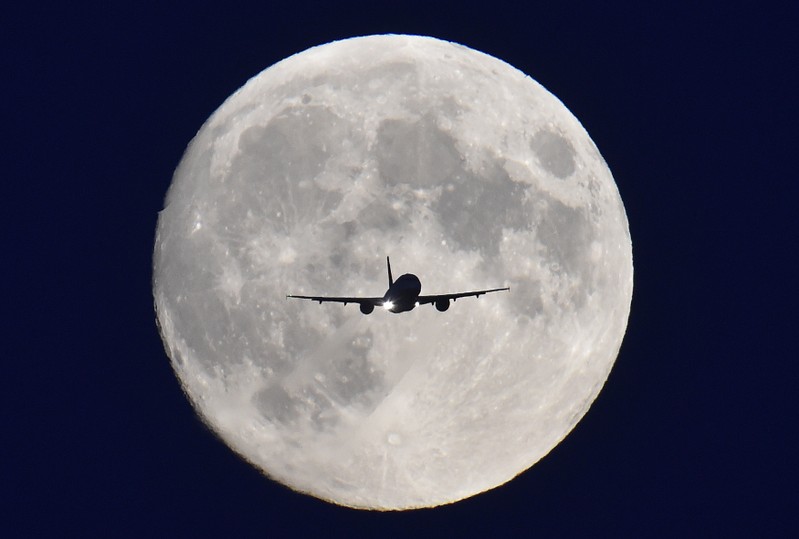 A passenger plane passes in front of the full moon as it makes a final landing approach to Heathrow Airport in west London