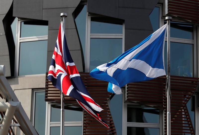 A Scottish flag flies next to British Union Jack flag outside the Scottish Parliament in Edinburgh