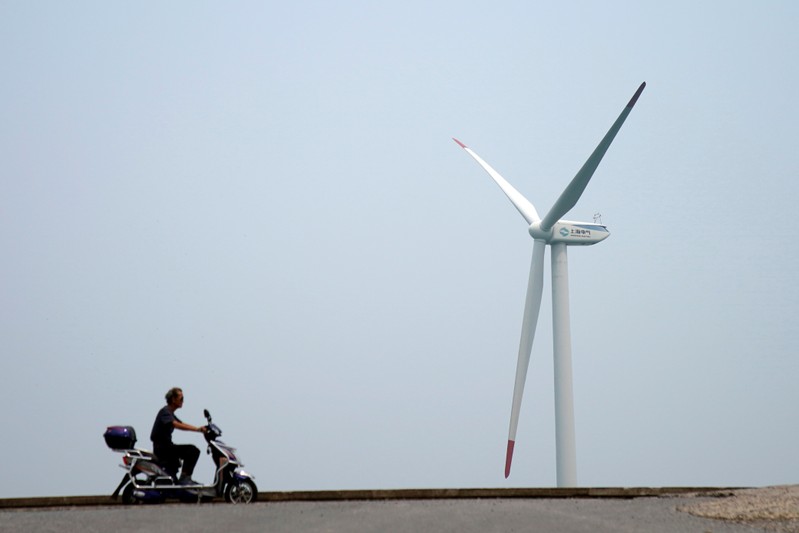 FILE PHOTO: A man rides an electric scooter past a wind turbine in Shanghai