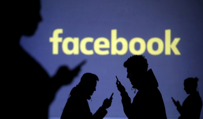FILE PHOTO: Silhouettes of mobile users are seen next to a screen projection of the Facebook logo in this picture illustration