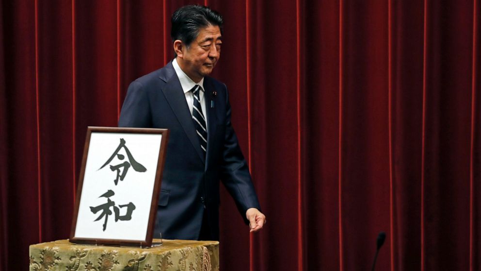 Japanese Prime Minister Shinzo Abe walks past the name of new era "Reiwa" on display at the Prime Minister's office in Tokyo, Monday, April 1, 2019.