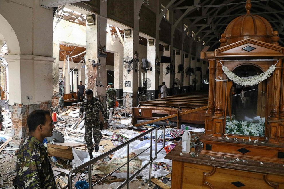 Sri Lankan security personnel walk past dead bodies covered with blankets amid blast debris at St. Anthony's Shrine following an explosion in the church in Kochchikade in Colombo, April 21, 2019.