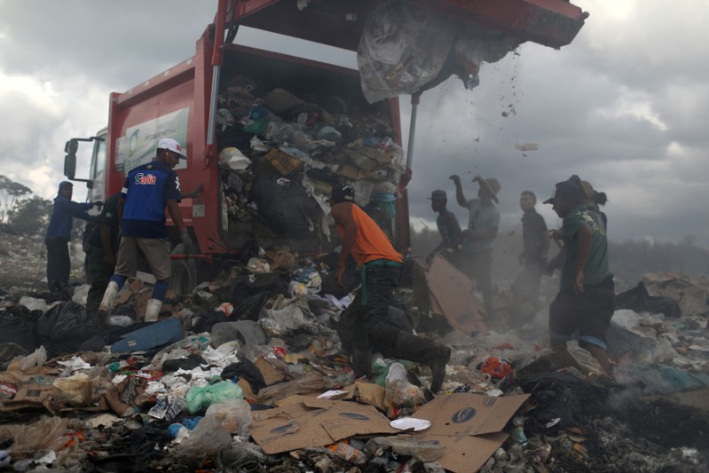 Venezuelan migrants wait while the rubbish truck unload at the garbage dump in the border city of Pacaraima