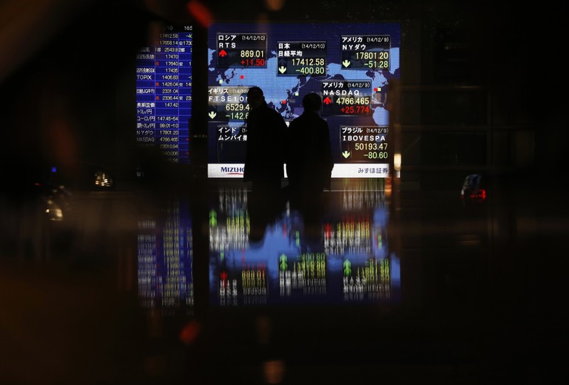 FILE PHOTO: Passersby are silhouetted in front of an electronic board displaying Japan's Nikkei average and various countries' stock price index outside a brokerage in Tokyo
