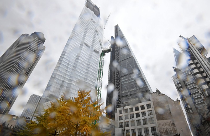 A tree covered in autumn foliage is seen with office skyscrapers around it during rainfall in the City of London, Britain