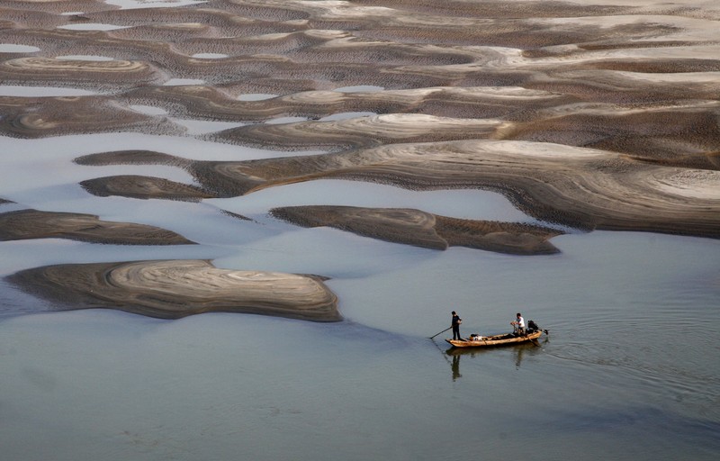 Two men row a boat past a partially dried-up riverbed on a section of the Yangtze River in Jiujiang