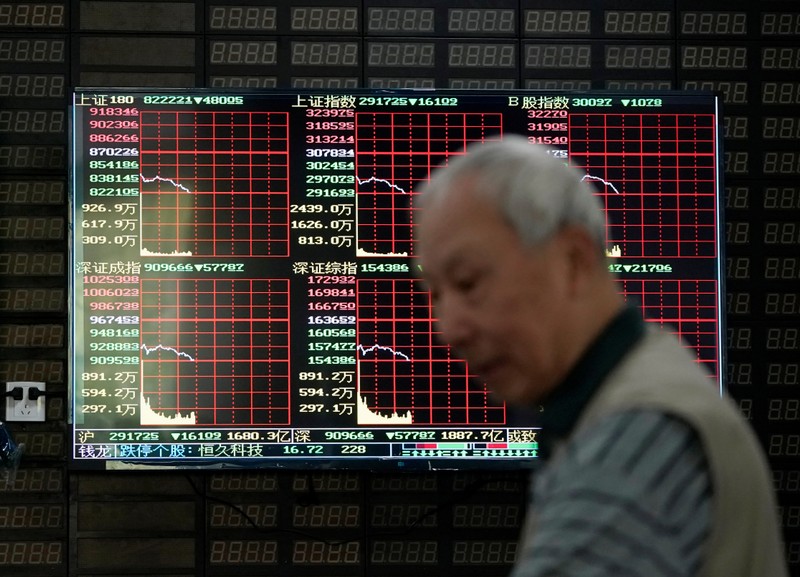FILE PHOTO: An investor walks past a screen displaying stock information at a brokerage house in Shanghai