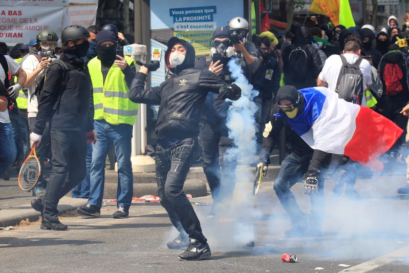 Tear gas floats around masked protesters during clashes with French riot police before the start of the traditional May Day labour union march in Paris