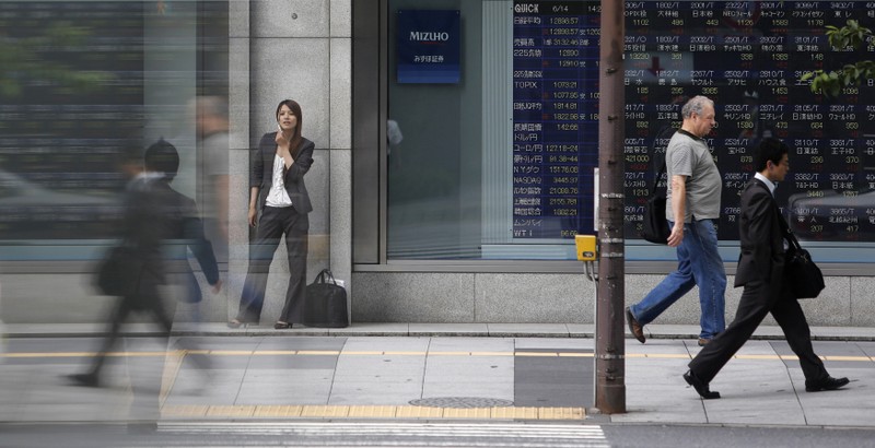 FILE PHOTO: Pedestrians walk past a stock quotation board displaying stock prices outside a brokerage, in Tokyo