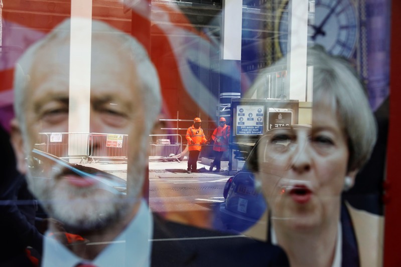 Wokers are reflected in the window of a betting shop with a display inviting customers to place bets on tbe result of the general election with images of Britain's Prime Minister Theresa May and opposition Labour Party leader Jeremy Corbyn, in London