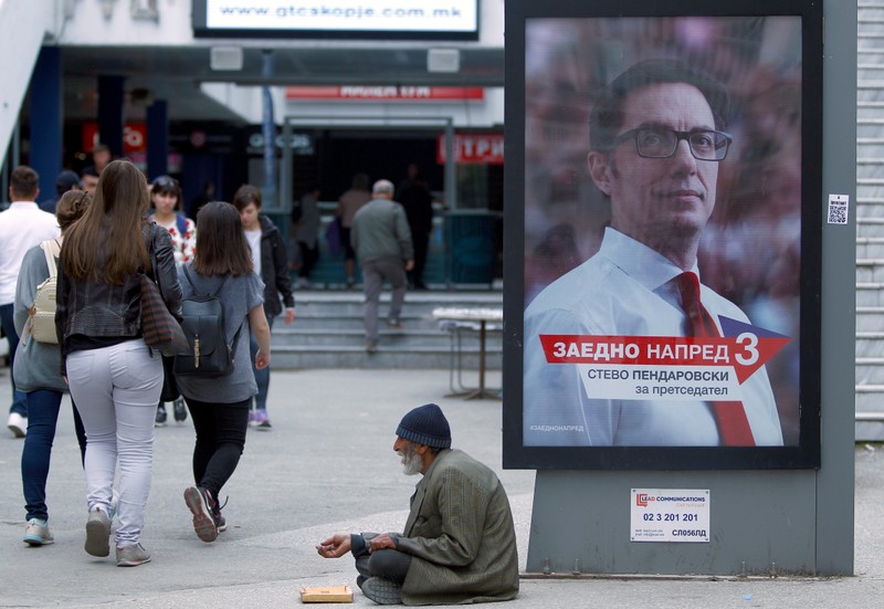A man begs for coins next to an election campaign poster of the ruling Social Democratic Union candidate Stevo Pendarovski before the presidential election on May 5 in Skopje