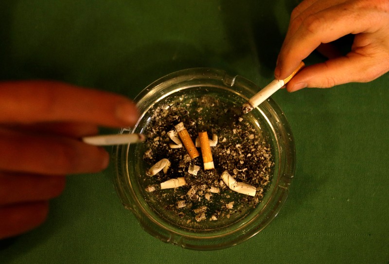 Men tap ashes off their cigarettes into an ashtray in a pub in Prague