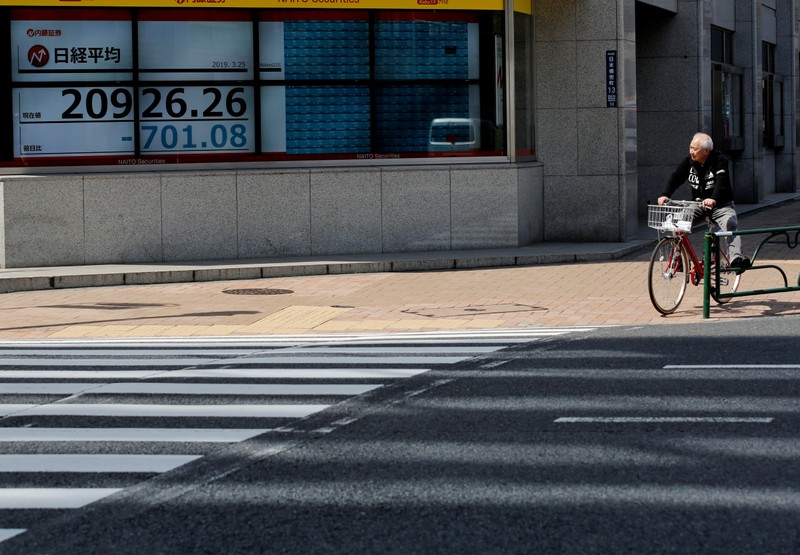 FILE PHOTO: A man in a bicycle stops in front of an electronic board showing the Nikkei stock index outside a brokerage in Tokyo