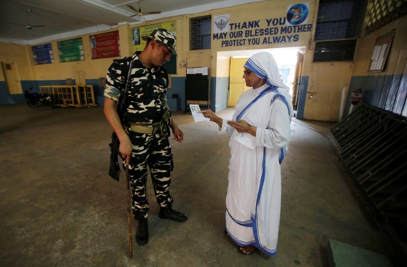A security personnel checks an identity card of a catholic nun from the Missionaries of Charity as she arrives to cast her vote at a polling station during the final phase of general election in Kolkata