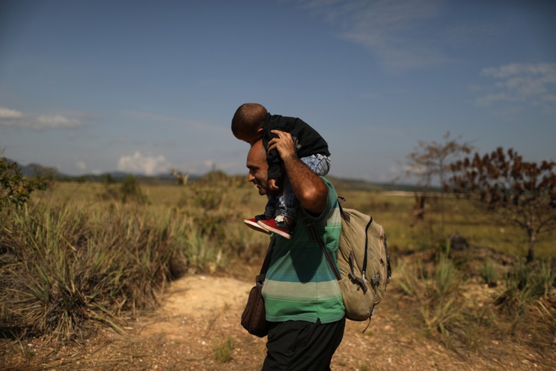 A Venezuelan migrant carrying a baby walks along a trail into Brazil in the border city of Pacaraima