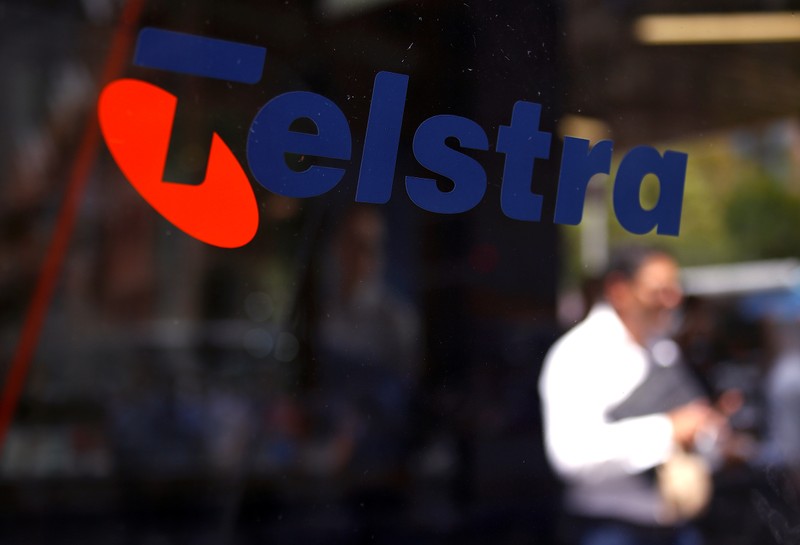 A man looks at his phone as he walks past a Telstra logo adorning a phone booth in the central business district of Sydney