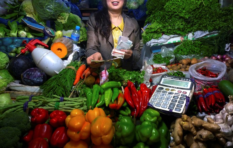 FILE PHOTO: A fruit and vegetable stall owner uses a calculator to work out prices for a customer at a small market in central Beijing