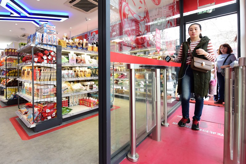Woman enters a JD.com's unmanned store with facial recognition technology, by scanning QR code with her phone on a detection machine at the store entrance in Xian, Shaanxi