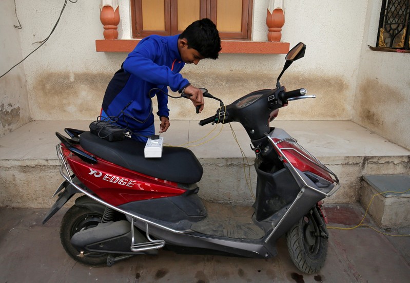 FILE PHOTO: A boy prepares to recharge his electric scooter outside his home in Ahmedabad
