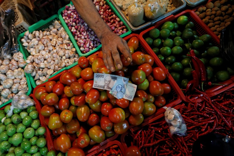 A vegetable vendor takes money from the customer during a transaction at a traditional market in Jakarta