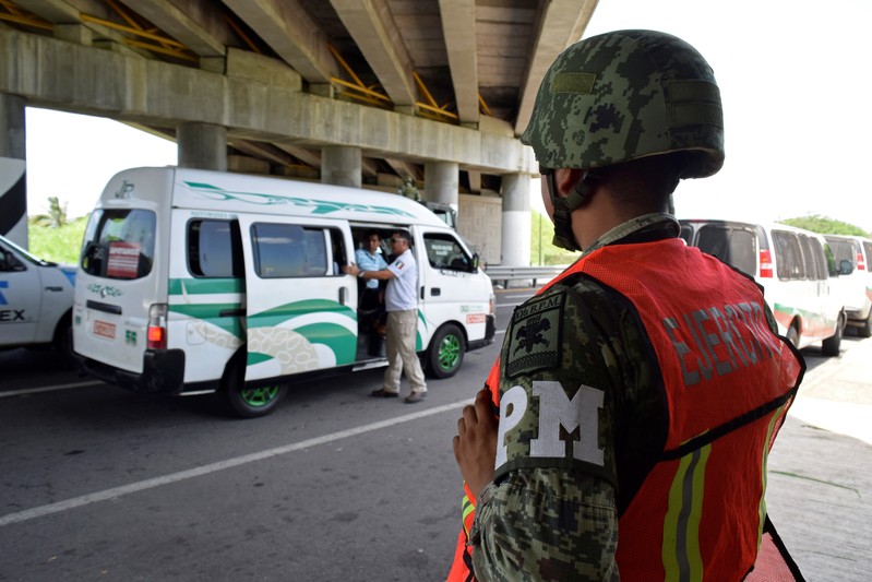 FILE PHOTO: A personnel of the National Migration Institute (INM) checks passenger's ID as a member of the Military Police keeps watch at a checkpoint on the outskirts of Tapachula