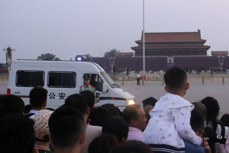 Paramilitary police officer stands guard in front of a police vehicle as people wait for the flag-raising ceremony held at Tiananmen Square during sunrise, in Beijing