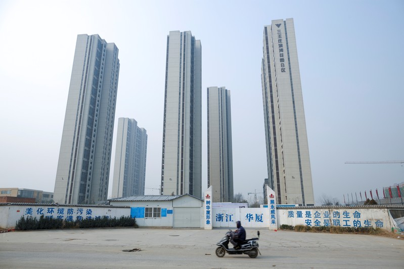 A man rides a scooter past apartment highrises that are under construction near the new stadium in Zhengzhou