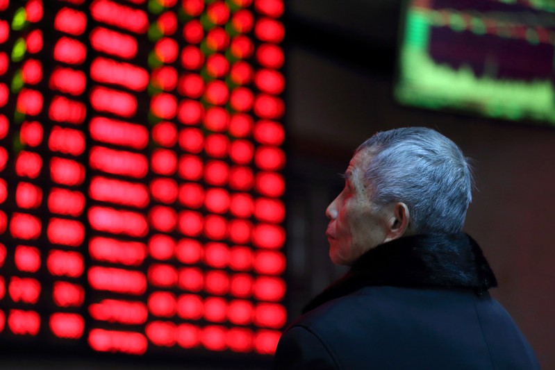 A man looks on in front of an electronic board showing stock information at a brokerage house in Nanjing