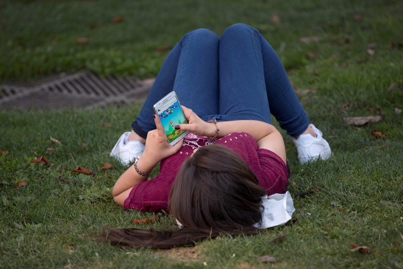 FILE PHOTO: A woman plays a game on her cell phone while lying on the grass in Madrid