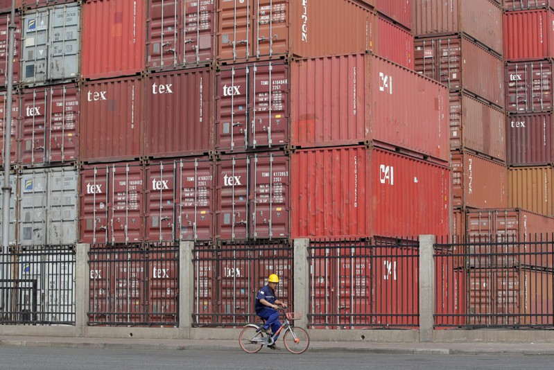 FILE PHOTO: A worker cycles past containers outside a logistics center near Tianjin Port