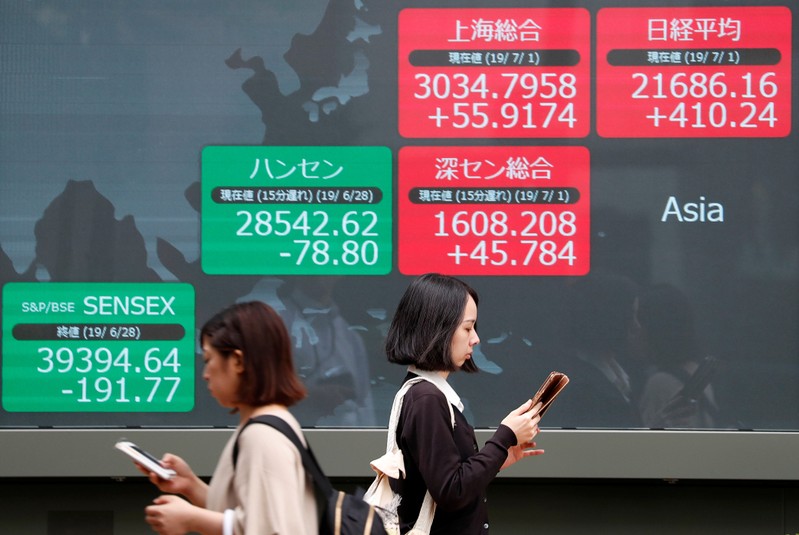 Passerbys walk past an electric screen showing Asian markets indices outside a brokerage in Tokyo