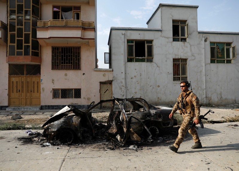 An Afghan security force walks past a burnt vehicle after Sunday’s attack at the site in Kabul, Afghanistan